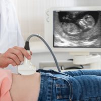 Cropped image of male doctor moving ultrasound probe on pregnant woman's belly