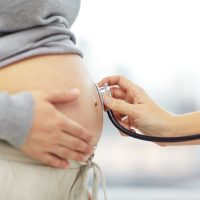 pregnancy, healthcare, people and medicine concept - close up of pregnant woman belly and doctor hand with stethoscope at medical appointment in hospital